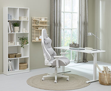 Svetlo siva gejmerska stolica, beli sto i polica u radnoj sobi