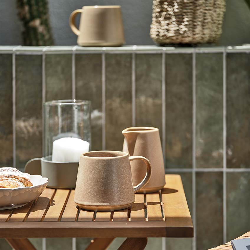Šolja za kafu i bokalčić za mleko na malom drvenom baštenskom stolu