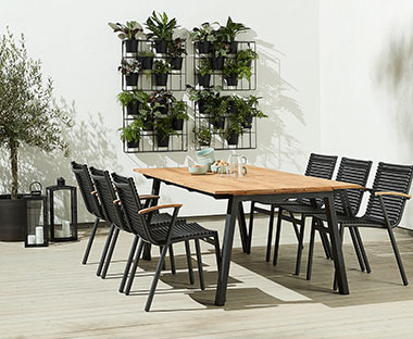 Baštenski set od stola i 6 baštenskih stolica u bašti pored zida sa visećim biljkama