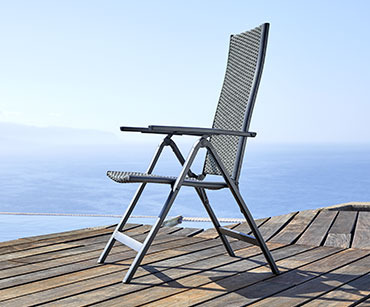 Crna baštenska stolica na drvenoj površini sa morem u pozadini