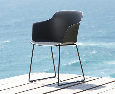 Crna plastična baštenska stolica na drvenoj površini i more u pozadini