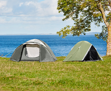 Dva šatora na travi pored drveća i vode