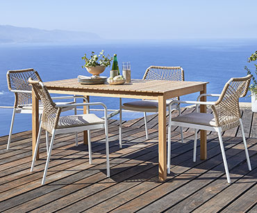 Drveni baštenski sto i 4 bele stolice na terasi sa pogledom na more