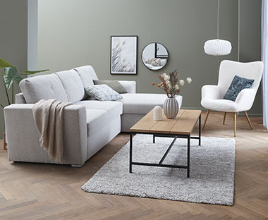 Svetlo siva sofa, drveni klub sto i bela fotelja u dnevnoj sobi