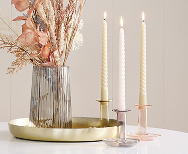 Tri svećnjaka sa visokim svećama pored zlatnog poslužavnika sa vazom