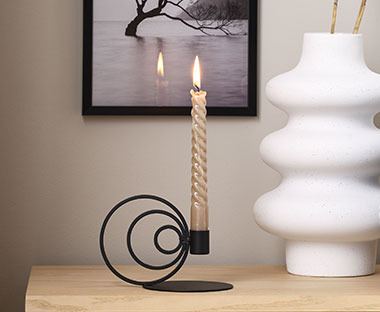 Crni metalni svećnjak sa bež svećom pored bele vaze