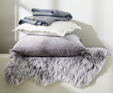 Ćebe i ukrasni jastuci na sivoj veštačkoj koži na svetloj podlozi