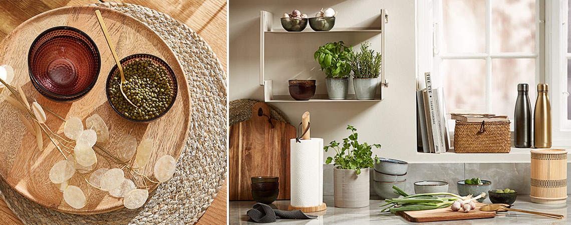 Staklene činije na pletenom podmetaču i kamene šoljice sa svežim začinskim biljkama na zidnoj polici u kuhinji