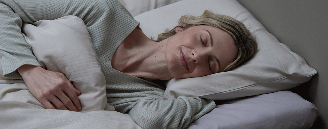 Žena spava na boku u krevetu s belim jastukom i jorganom