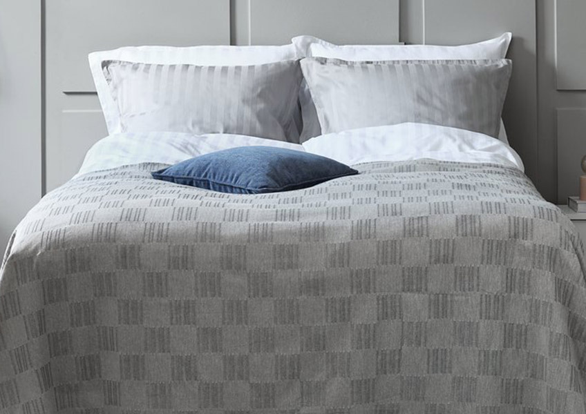 Sivi prekrivač i sive i bele jastučnice na bračnom krevetu