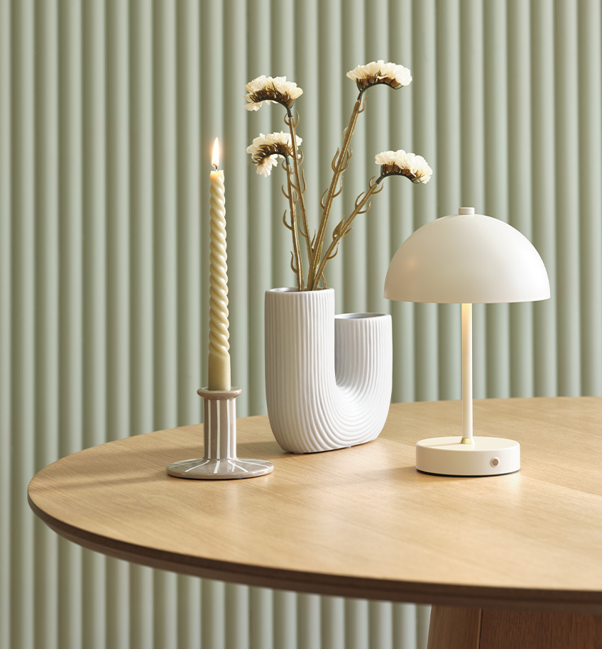 Elegantna lampa na baterije sa mesinganim detaljem, vaza i svećnjak na drvenom stolu