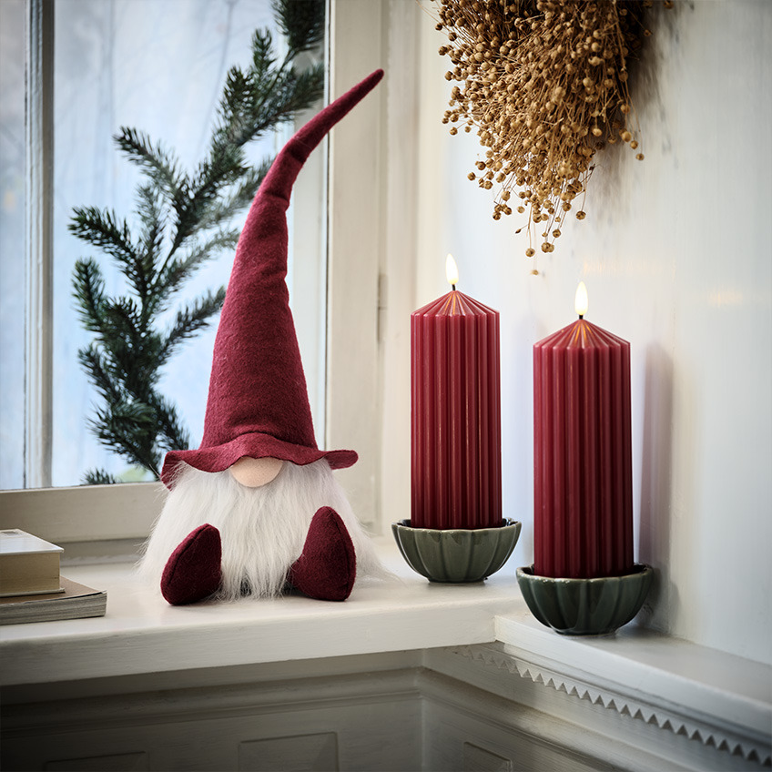 Skandinavski božićni patuljak na prozorskoj dasci pored velikih crvenih sveća