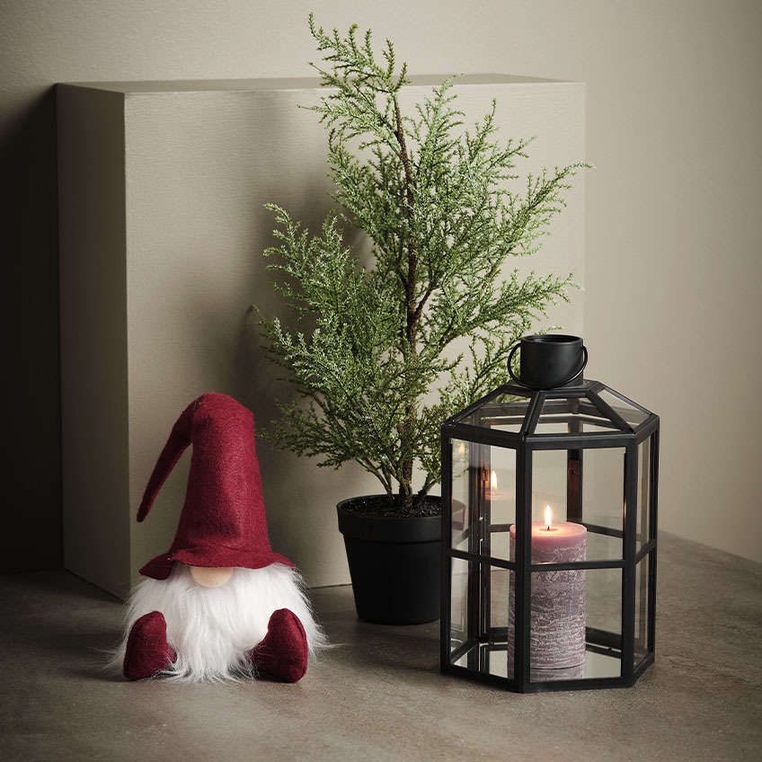 Skandinavski božićni vilenjak pored veštačke biljke i fenjera
