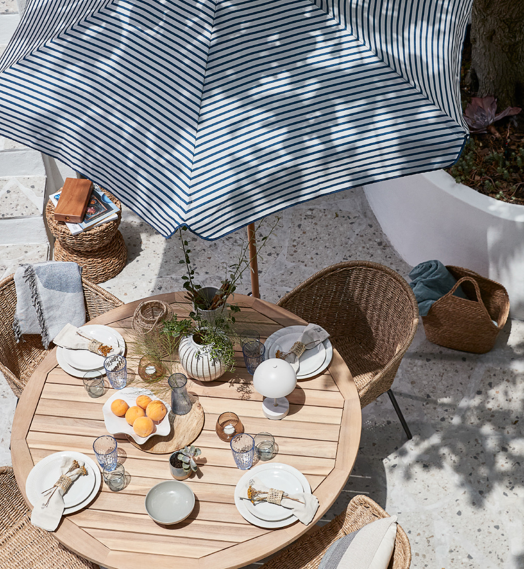 Postavljen baštenski sto i stolica ispod prugastog suncobrana na terasi