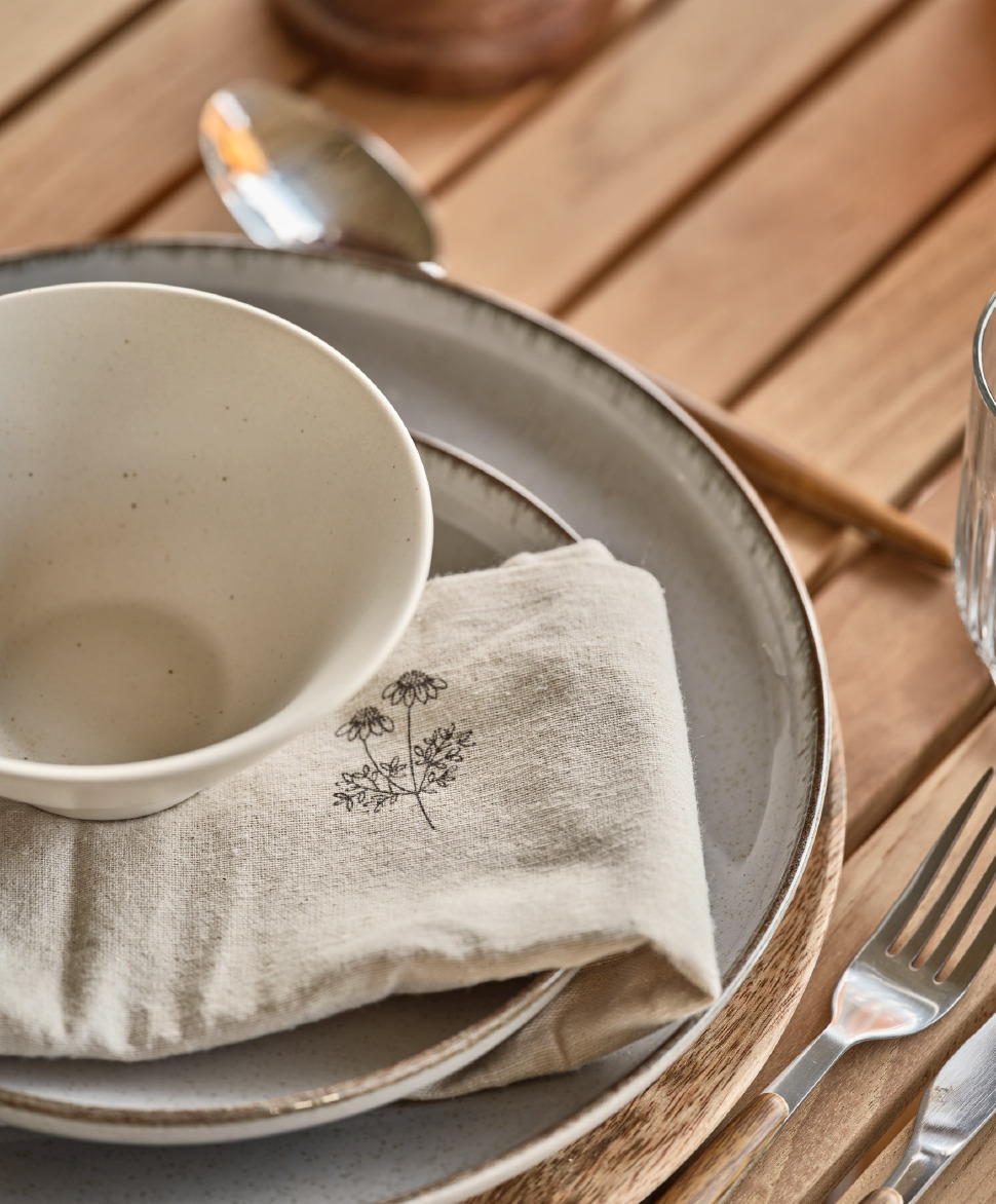 Sivi tanjiri, lepa platnena salveta i bela činija na drvenom stolu