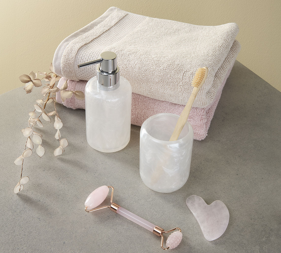 Peškir boje peska i roze peškiri pored držača četkice za zube, dozera tečnog sapuna i valjak za lice i masažnog kamena