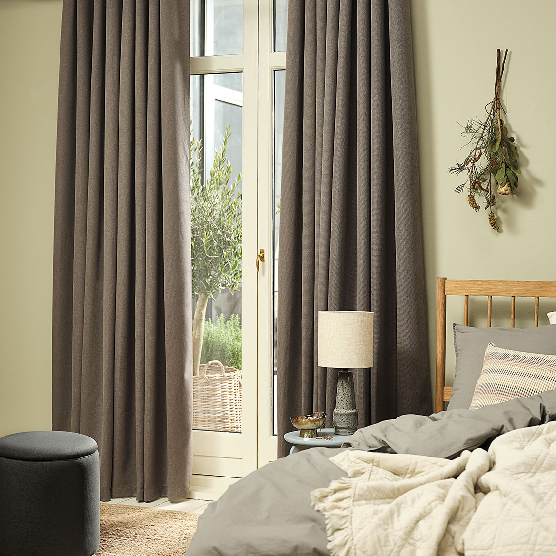 Warm grey dimming curtains hung by a large window in a bedroom 