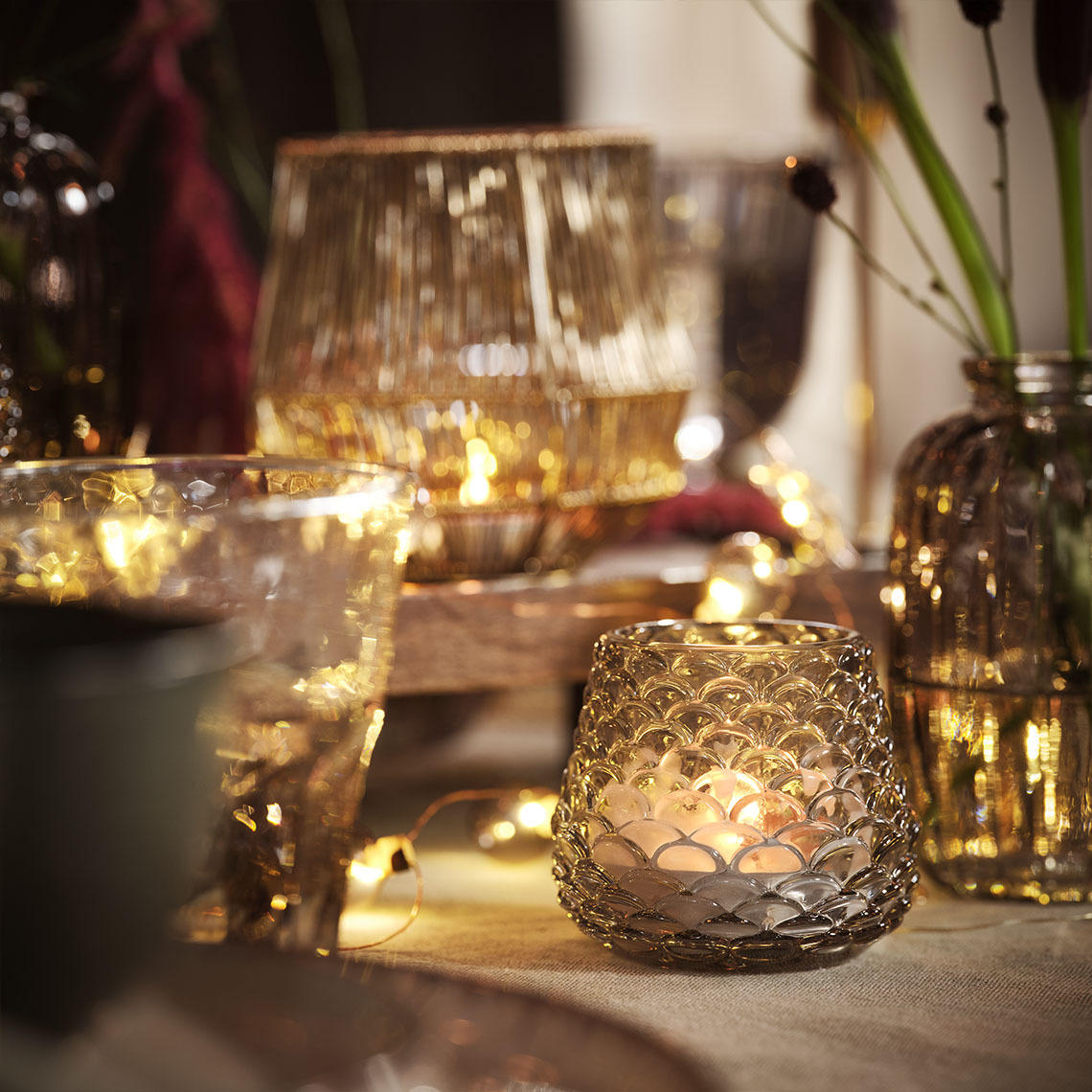 Trpezarijski sto osvetljen svećama i svećnjacima i lampicama u nizu