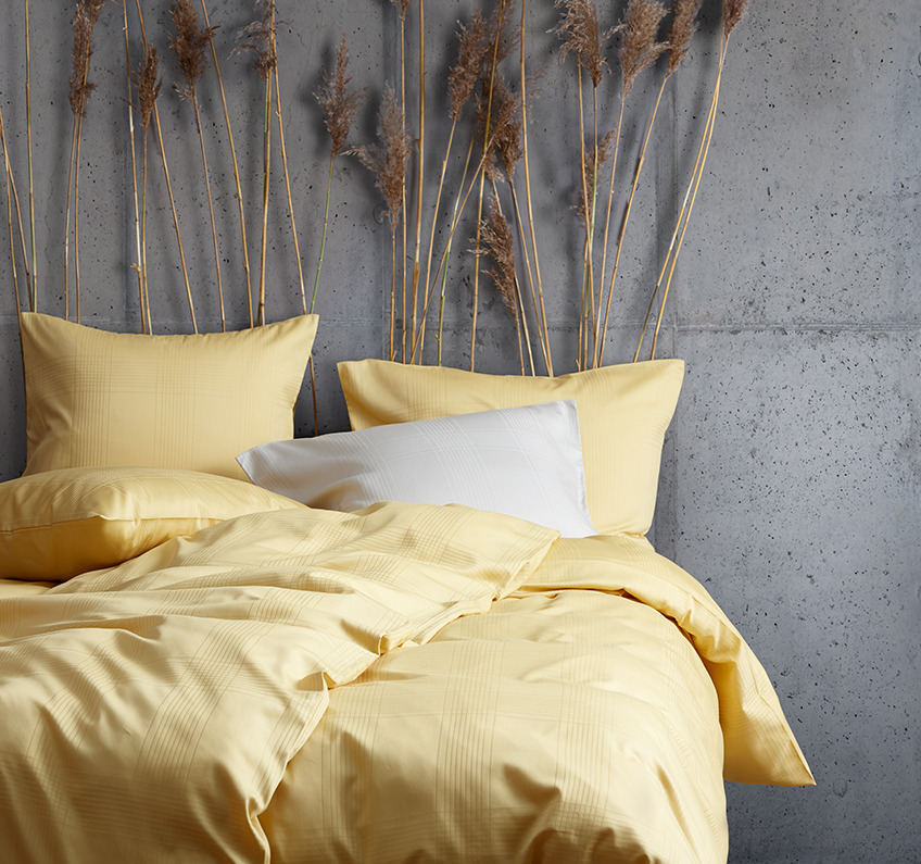 Žuta posteljina od Mirne boje i lagani uzroci inspirišu vas da se isključite, opustite i prepustite se Žuta posteljina napravljena od 51% recikliranog poliestera i 49% pamučnog satena u spavaćoj sobi betonskih zidova