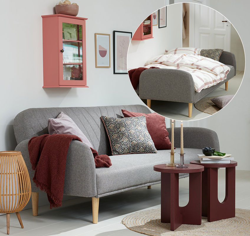 Zidni ormarić u roze boji, sivi kauč na razvlačenje i bordo stočići