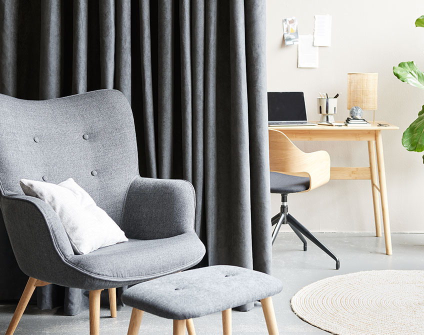 Sive zavese razdvajaju home office sa stolom i radnom stolicom od dnevne sobe sa foteljom