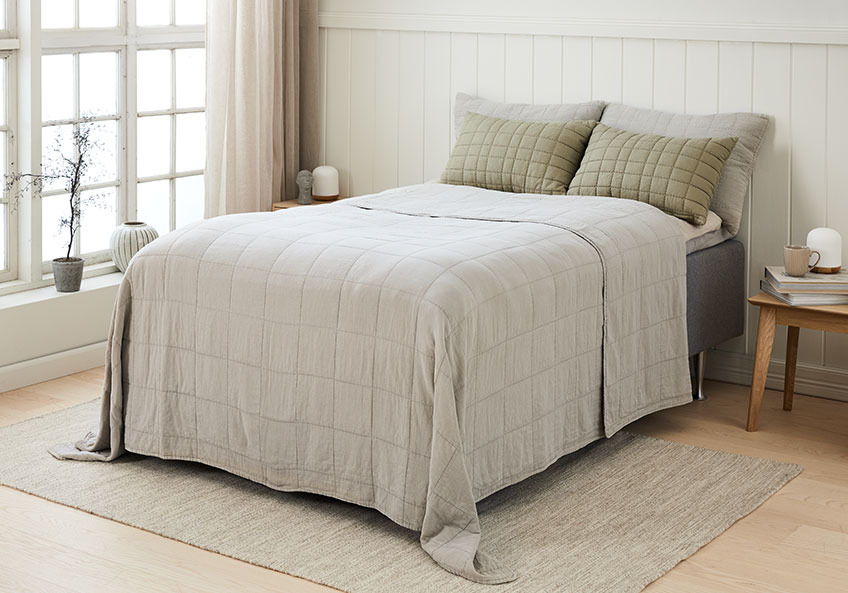 Krevet sa štepanim ćebetom i odgovarajućim jastucima za leđa u svetloj spavaćoj sobi