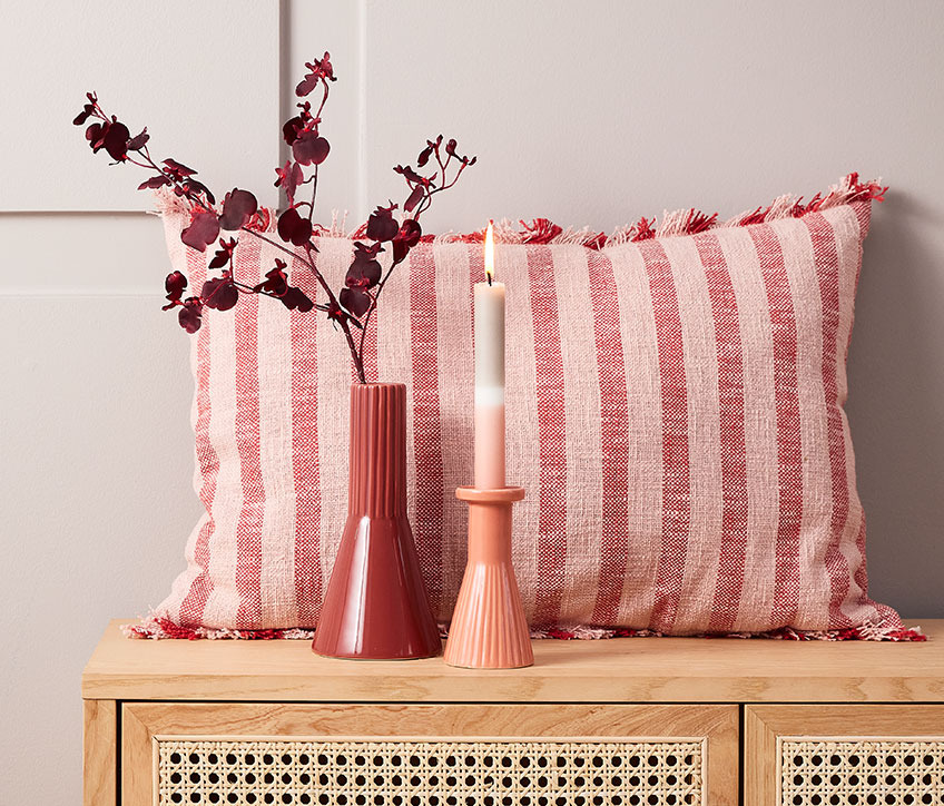 Ukrasni prugasti jastuk iza crvene vaze i svećnjaka sa prugastom svećom