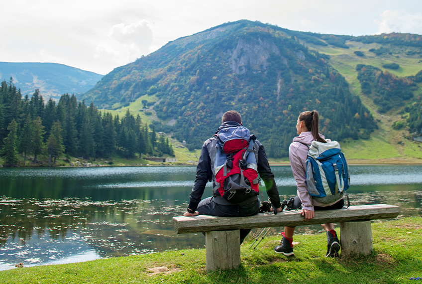 Muškarac i žena sede na klupi i gledaju u planine i jezero