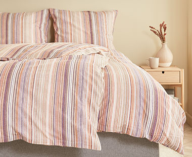 Posteljina sa ljubičastim, belim i narandžastim linijama na krevetu u spavaćoj sobi
