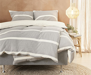 Sivo krem pamučna posteljina na krevetu pored noćnog ormarića i lustera