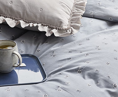 Plava posteljina sa cvetićima na krevetu i poslužavnik sa kafom