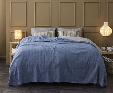Plavi prekrivač na bračnom krevetu pored noćnih ormarića u spavaćoj sobi